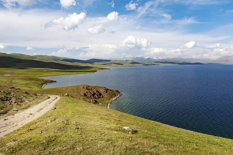 a road on the shore of the deep blue Song Kul lake