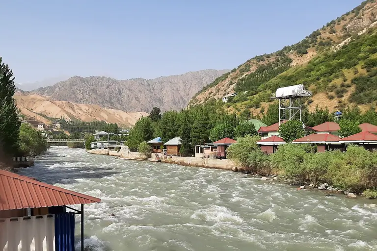 The Varzob River, originating from the Fan Mountains and flowing towards Dushanbe, is a cherished summer destination for Tajiks seeking cool relief. Along its banks are tourist complexes, featuring quaint riverside houses. In the distance, the dry mountains of the Varzob valley complete the landscape.