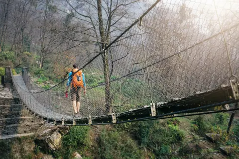 Tourist with backpack crossing suspension footbridge at Himalayas
