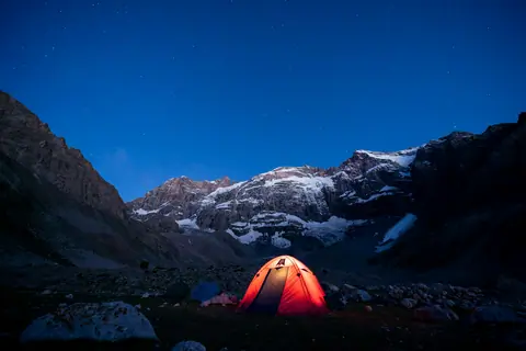 An illuminated tent at night under the Merali Peak headwall, deep in the Fann Mountains of Tajikistan.
