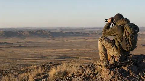 Wildlife watcher searching the vast landscapes of the Gobi Desert with binoculars