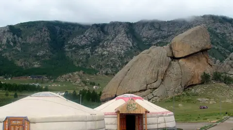 2 mongol yurts on a green pasture, on the feet of big rocks and rocky mountains, under cloudy day