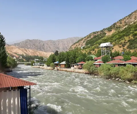 The Varzob River, originating from the Fan Mountains and flowing towards Dushanbe, is a cherished summer destination for Tajiks seeking cool relief. Along its banks are tourist complexes, featuring quaint riverside houses. In the distance, the dry mountains of the Varzob valley complete the landscape.
