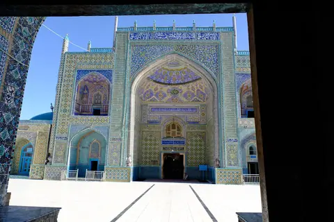 View of the Blue Mosque in Mazar-e Sharif, with its turquoise domes, arched entrances, and walls covered in intricate blue tilework.