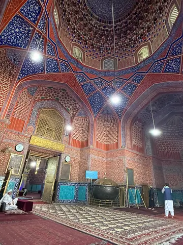 Interior of the coupole of the Blue Mosque, featuring high vaulted ceilings, intricately tiled walls in shades of blue and white, and a large prayer hall carpeted in red, with soft natural light filtering through arched windows.