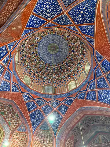 Interior of the coupole of the Blue Mosque, featuring high vaulted ceilings, intricately tiled walls in shades of blue and white, and a large prayer hall carpeted in red, with soft natural light filtering through arched windows.