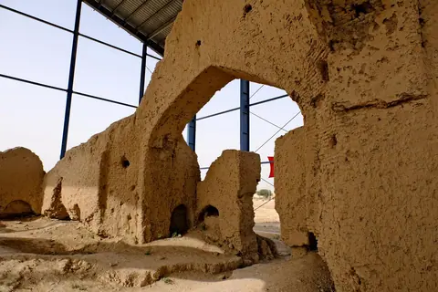 Ruins of an ancient mud-brick structure in Balkh, Afghanistan, believed to be the site of Rumi’s childhood home. The partially exposed foundations lie in a dusty, open area, surrounded by sparse grass and scattered stones, evoking the poet's spiritual origins.