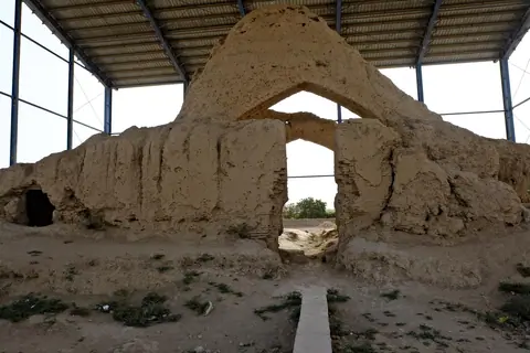 Ruins of an ancient mud-brick structure in Balkh, Afghanistan, believed to be the site of Rumi’s childhood home. The partially exposed foundations lie in a dusty, open area, surrounded by sparse grass and scattered stones, evoking the poet's spiritual origins.