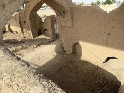 Ruins of an ancient mud-brick structure in Balkh, Afghanistan, believed to be the site of Rumi’s childhood home. The partially exposed foundations lie in a dusty, open area, surrounded by sparse grass and scattered stones, evoking the poet's spiritual origins.