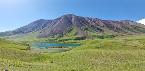 A turquoise blue lake surrounded by green meadows where Kyrgyz nomads set up their yurts in summer. The lake often reflects Lenin Peak, one of the 7,000-meter peaks of the Pamir Mountains.