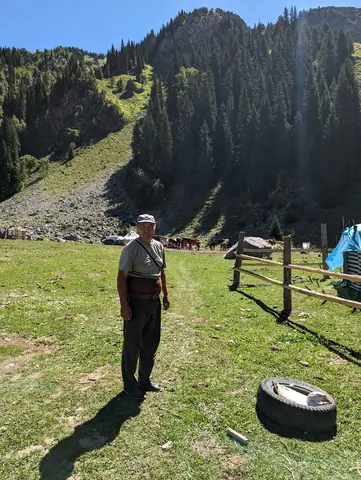 During summer time, green meadows and forest, a nomad is standing near his camp