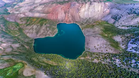 Aerial view of a deep blue lake surrounded by rocky, green hills.