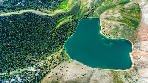 Aerial view of a teal lake bordered by forest and dry hills.