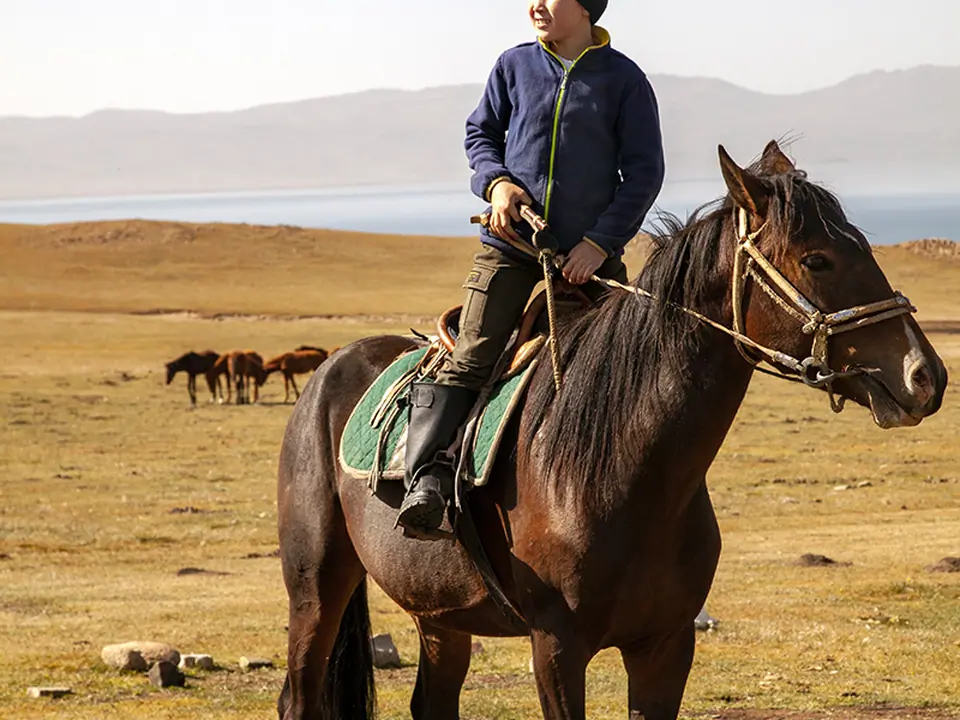Young boy riding a horse in Son Kul img