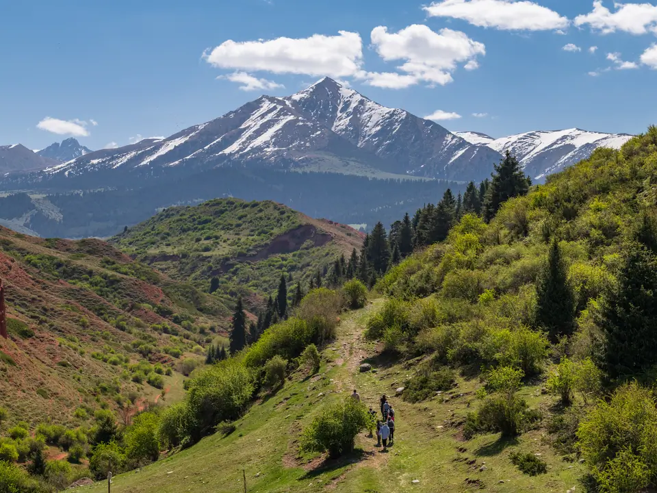The snowy Jeti Oguz peak stand in the middle above red canyons and green juniper and fir-tree forests