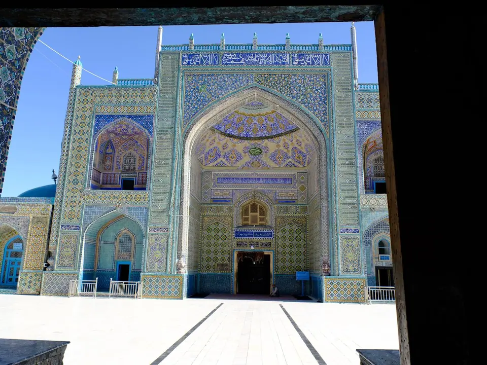 View of the Blue Mosque in Mazar-e Sharif, with its turquoise domes, arched entrances, and walls covered in intricate blue tilework.