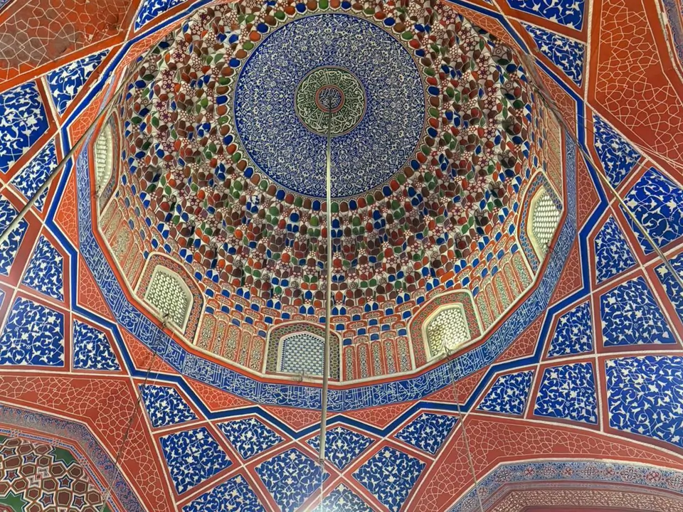 Interior of the coupole of the Blue Mosque, featuring high vaulted ceilings, intricately tiled walls in shades of blue and white, and a large prayer hall carpeted in red, with soft natural light filtering through arched windows.