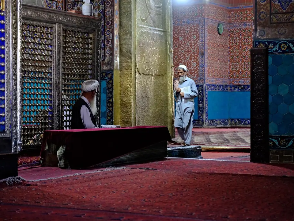 Interior of the Blue Mosque, featuring high vaulted ceilings, intricately tiled walls in shades of blue and white, and a large prayer hall carpeted in red, with soft natural light filtering through arched windows.