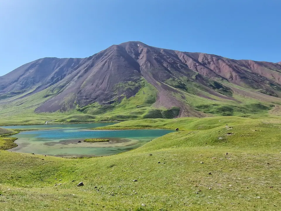 A turquoise blue lake surrounded by green meadows where Kyrgyz nomads set up their yurts in summer. The lake often reflects Lenin Peak, one of the 7,000-meter peaks of the Pamir Mountains.