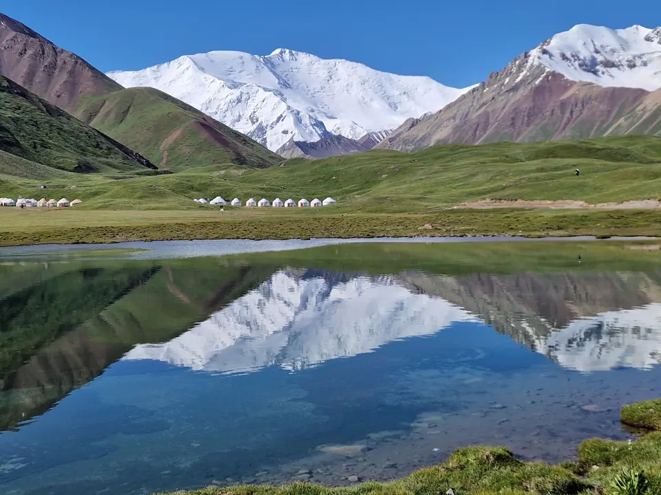 A turquoise blue lake surrounded by green meadows where Kyrgyz nomads set up their yurts in summer. The lake often reflects Lenin Peak, one of the 7,000-meter peaks of the Pamir Mountains.