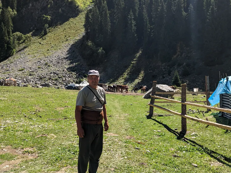 During summer time, green meadows and forest, a nomad is standing near his camp