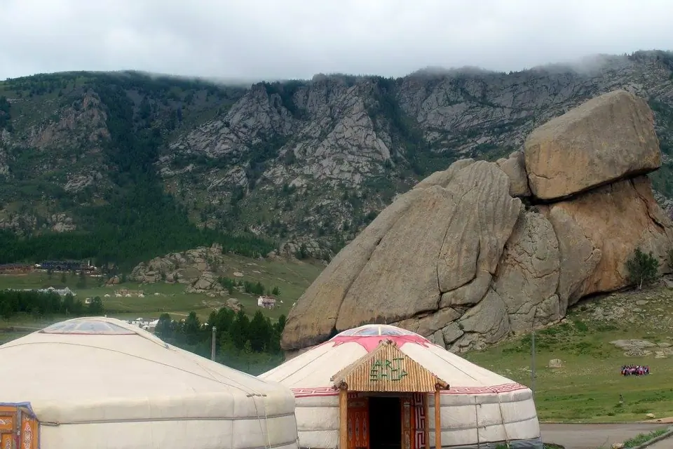 2 mongol yurts on a green pasture, on the feet of big rocks and rocky mountains, under cloudy day