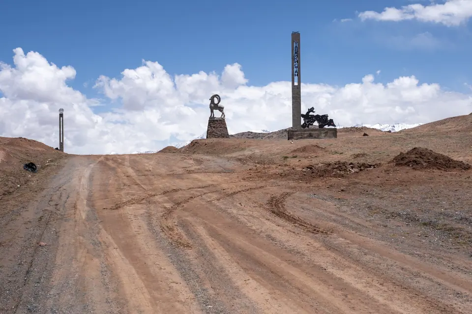 A dirty road at the Kyzyl Art pass at 4288 m. alt. with a statue of a marco polo wild sheep and a welcome statue in Tajikistan