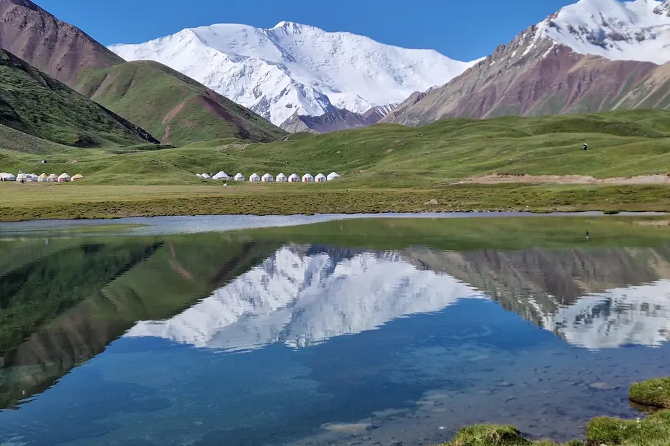 A turquoise blue lake surrounded by green meadows where Kyrgyz nomads set up their yurts in summer. The lake often reflects Lenin Peak, one of the 7,000-meter peaks of the Pamir Mountains.