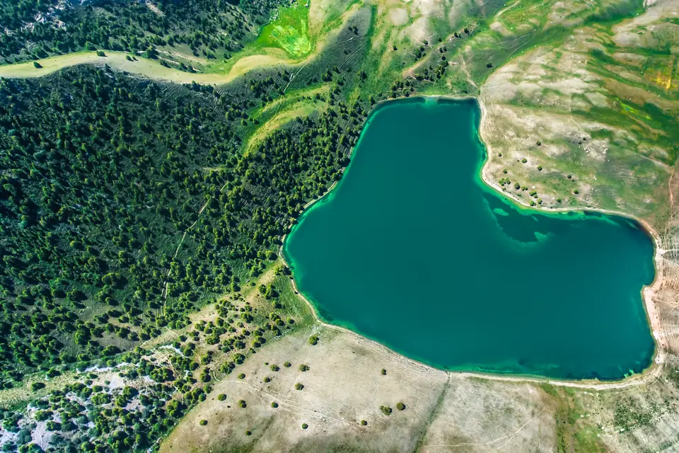 Aerial view of a teal lake bordered by forest and dry hills.